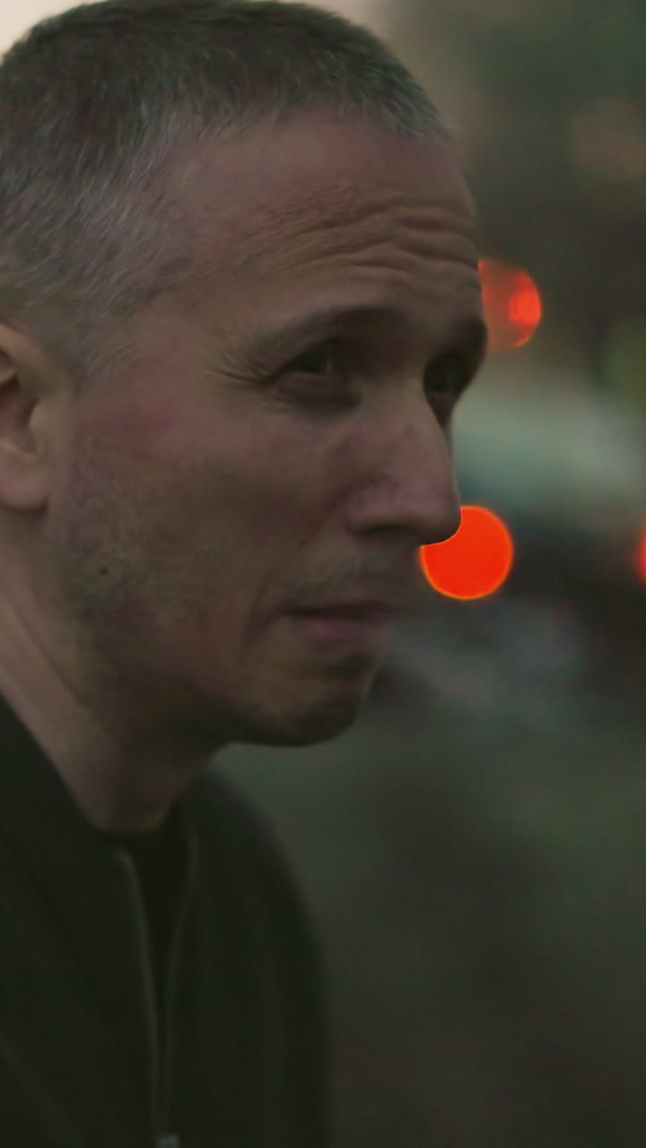 A man in a green jacket is captured in a dimly lit scene, smoking a cigarette with smoke visibly escaping from his nose and mouth