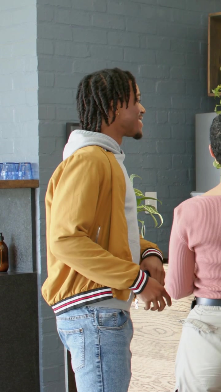 Vertical video: Coming to cafe counter, man in yellow jacket with phone, woman in pink top ordering