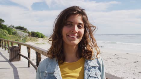 Portrait-of-happy-mixed-race-woman-standing-on-sunny-promenade-by-the-sea-smiling