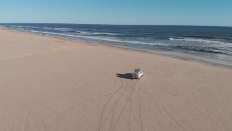 drone video aéreo de un jeep blanco conduciendo en la arena en la costa esquelética de namibia, áfrica. aventurero y mochilero mirando el océano y el mar mientras está de pie en un jeep. arena marrón y olas de agua. drone siguiendo furgoneta y jeep.