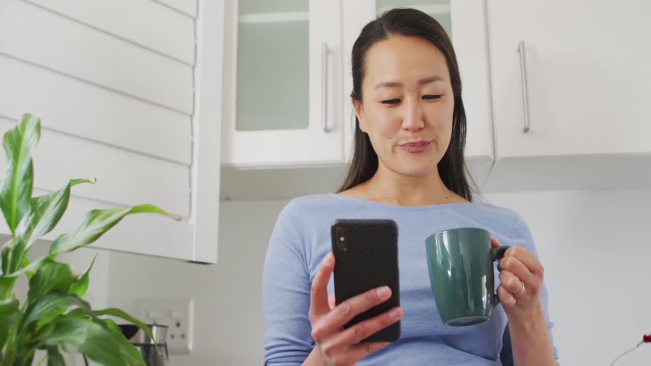 행복한 아시아 여성이 커피를 마시고 부 ⁇ 에서 스마트폰을 사용하고 있습니다.