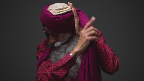 fotografía de iluminación de estudio de baja clave de un anciano sikh con barba atando tela para turbante contra un fondo oscuro tomada en tiempo real