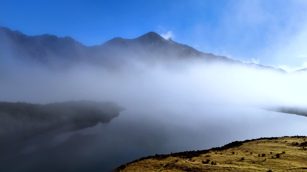 A serene view of fog enveloping Moke Lake, with mountains in the background and clear blue skies above