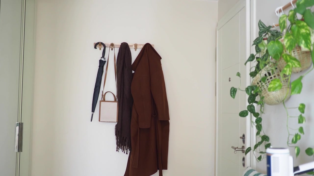 Cappotto marrone e accessori appesi a un appendiabiti a muro nell'ingresso.