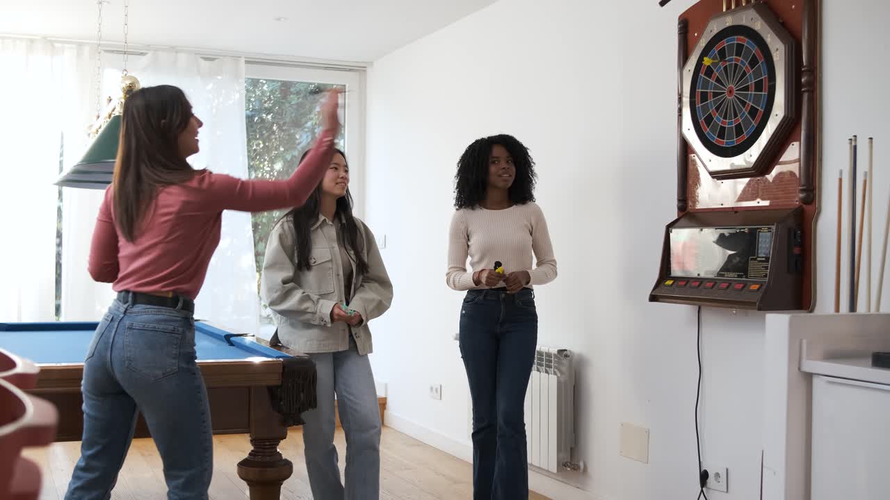 Happy woman playing game of dart with female friends in game room