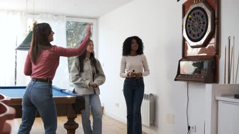 happy woman playing game of dart with female friends in game room