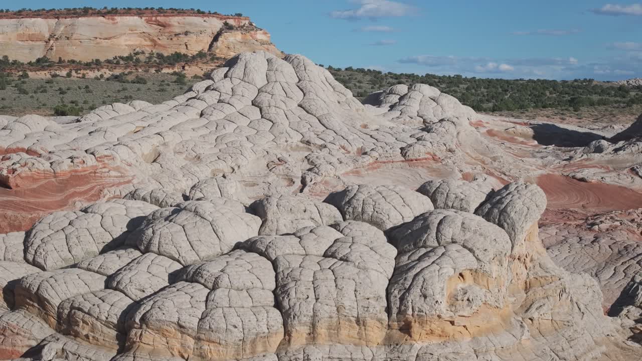 A drone raising altitude to reveal the unique sandstone rock features of White Pocket Arizona at midday surrounded by sandy desert