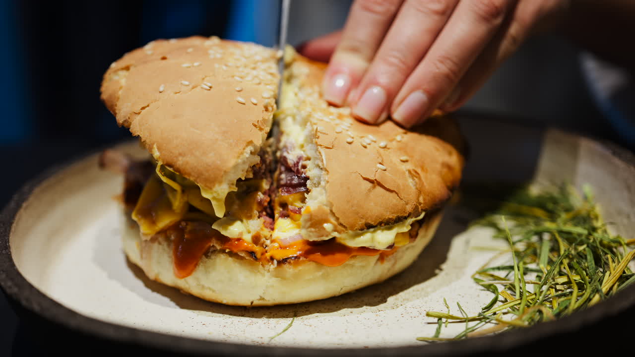 Close up of a woman cutting a burger in half on a plate at a restaurant