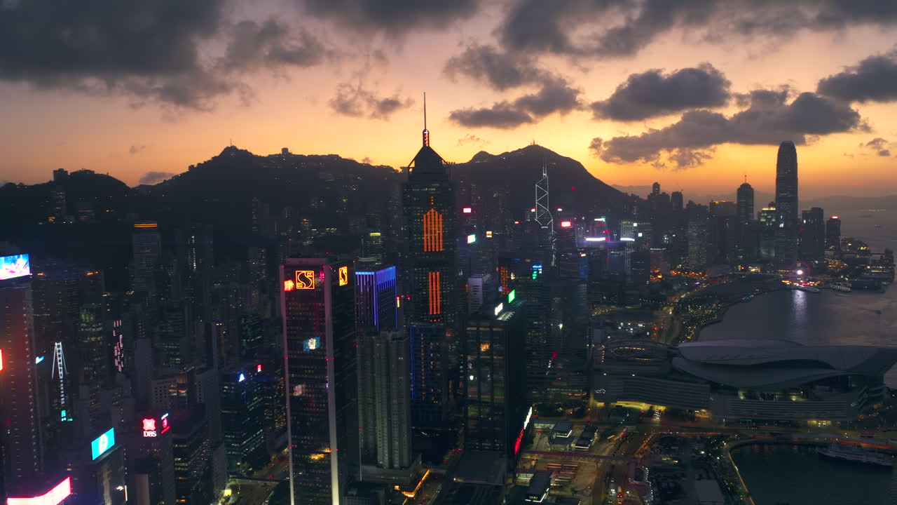 Widok z lotu ptaka na słynną panoramę Hongkongu podczas zachodu słońca, za sylwetką pasma górskiego – Piękne miasto z drapaczami chmur, billboardami i nabrzeżem