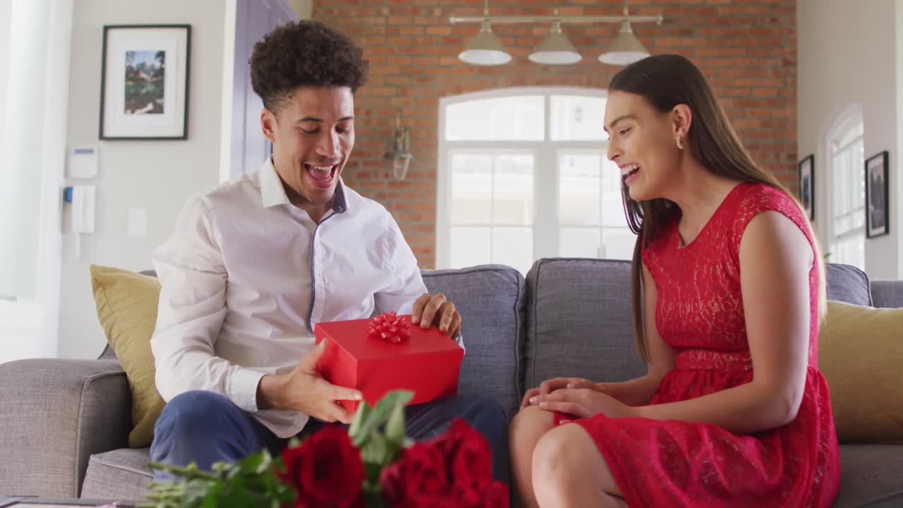 Happy biracial couple celebrating valentine's day giving presents at home