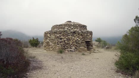 old stone hut near megalithic trail with misty mountain in background near roses, catalonia, spain