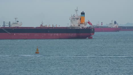 Grandes-Buques-De-Carga-En-El-Estrecho-De-Singapur,-Barcos-De-La-Autoridad-Gubernamental-Navegando,-Inspeccionando-Los-Productos-Aduaneros-Y-Documentándolos-Antes-De-Que-Lleguen-Al-Interior.