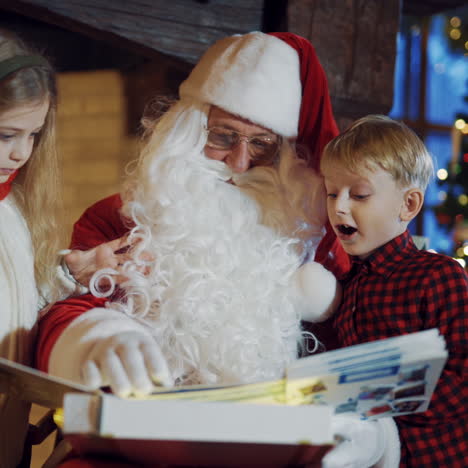 little children with santa looking into interesting photo album. santa claus in traditional red costume sitting in the room and turning pages in big album together with boy and girl.