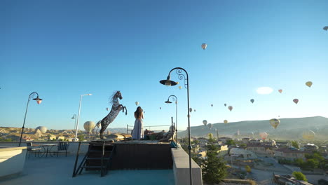 Woman-on-Terrace-Looking-at-Cappadocia-Landscape-and-Hot-Air-Balloons,-Turkey