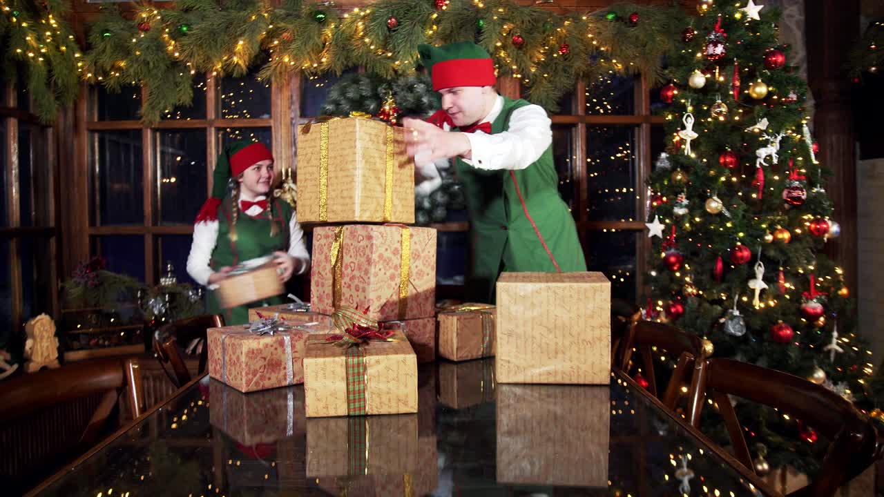 Presents for xmas holidays. Cheerful elves putting gift boxes on the table near Christmas tree in decorated room