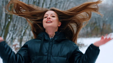 caucasian woman in black jacket walks in the park in winter. smiling lady turns and waves her long hair. blurred backdrop.