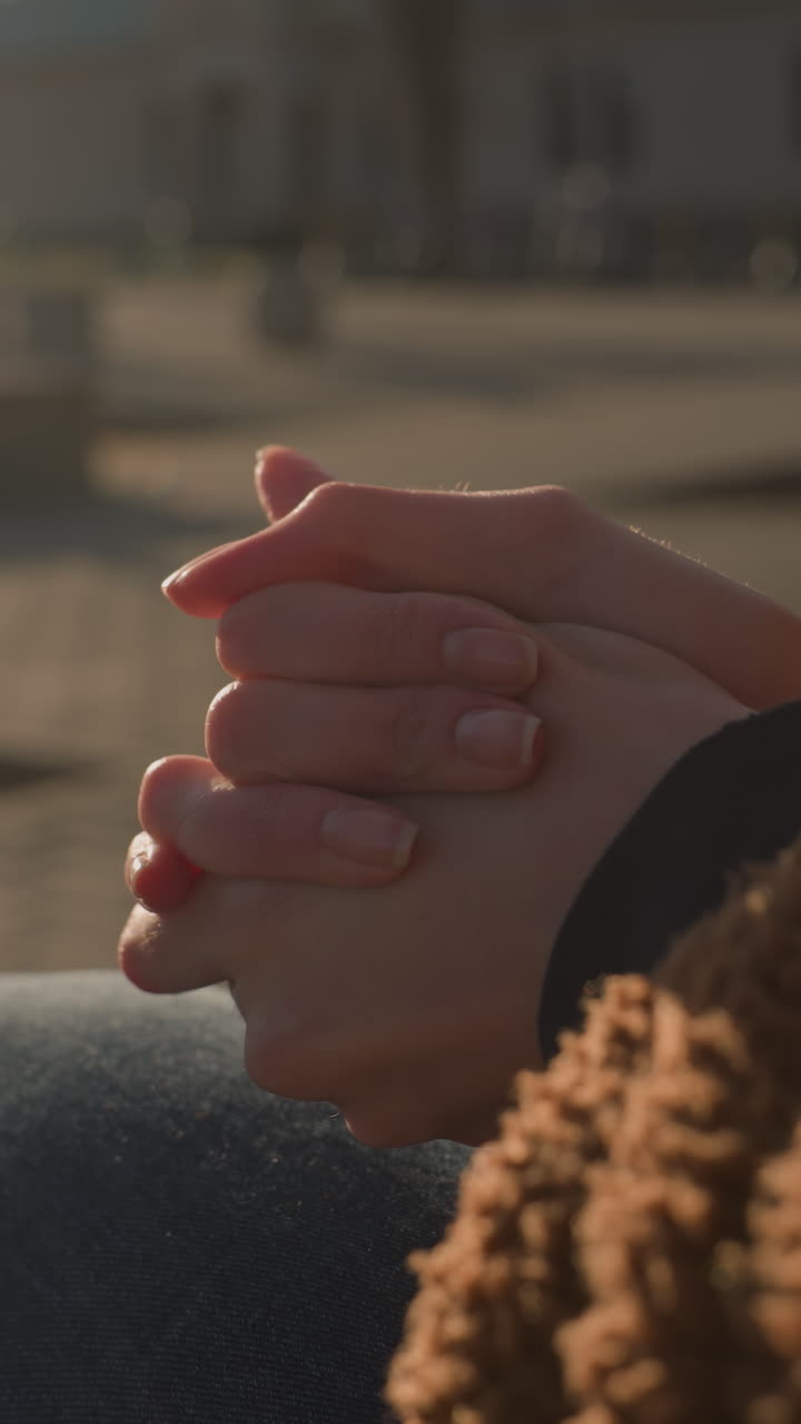 primer plano de una persona sentada con la cara no visible, con pantalones vaqueros azules y un abrigo marrón. las manos están fuertemente juntas, lo que sugiere un pensamiento profundo y meditación