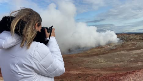 blonde tourist woman taking pictures with a reflex of a fumarole in gunnuhver, iceland