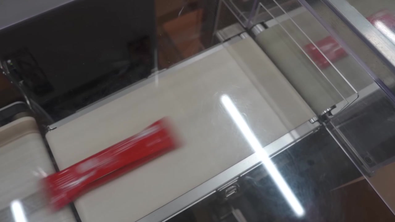Singola bustina rossa sigillata che poggia su un nastro bianco tra barre luminose brillanti in una linea di confezionamento