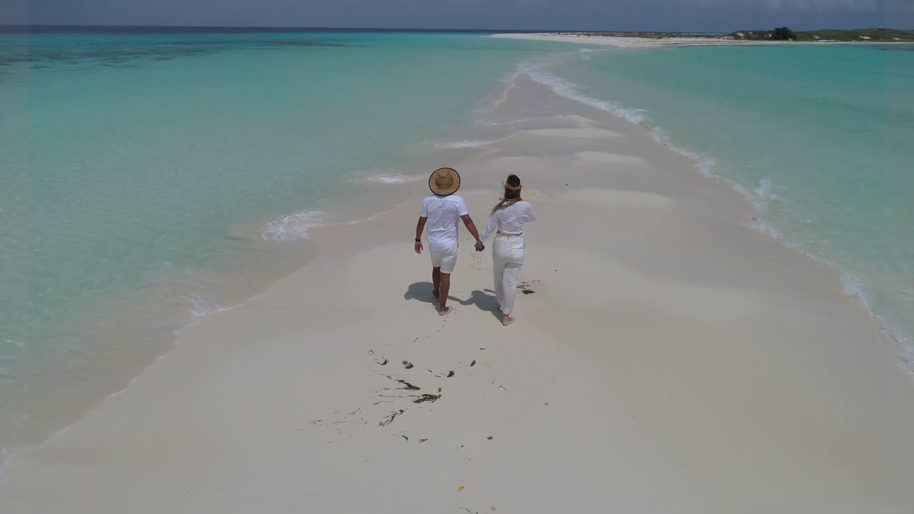 Couple holding hands walking on the white sandbar of Cayo de Agua, Los Roques Archipelago, Venezuela, with turquoise Caribbean waters