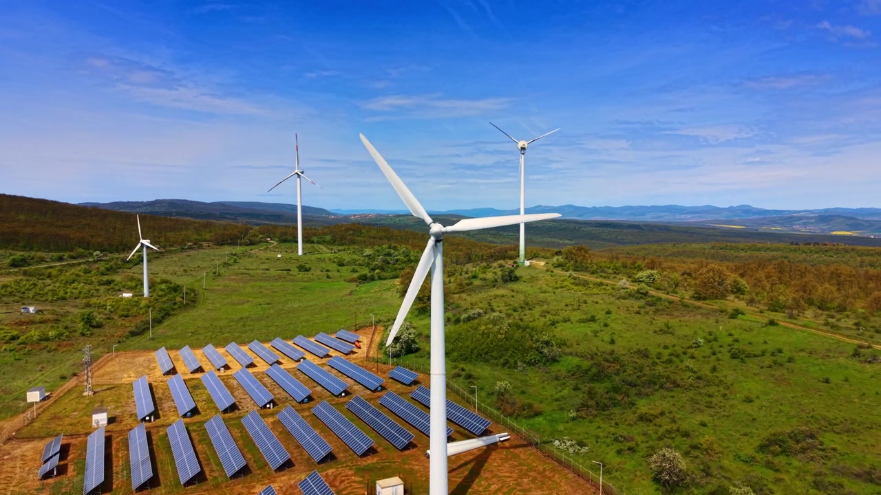 Aerogeneradores y paneles solares en uso. Los aerogeneradores se alzan en un campo verde con paneles solares dispuestos debajo de ellos durante un día soleado.