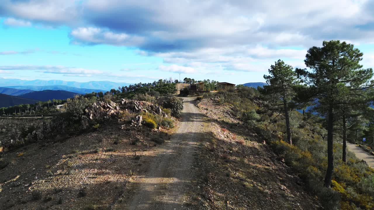 Voo de drone sobre estrada de terra sinuosa cruzando cume de montanha entre densa floresta de pinheiros na Extremadura, Espanha. Conceito de paisagem rural cênica e gestão florestal