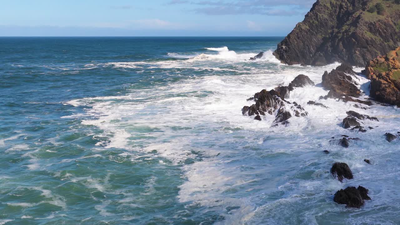 Dynamic ocean waves crash against rocky cliffs under bright daylight, showcasing the power and beauty of nature