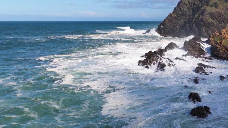 Dynamic ocean waves crash against rocky cliffs under bright daylight, showcasing the power and beauty of nature
