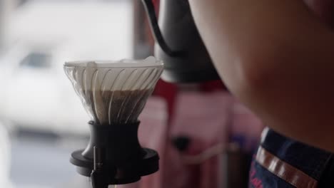 close up view in slow motion of a gooseneck kettle pouring hot water in a v60 dripper with coffee grounds.