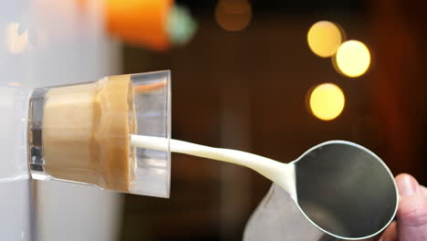 4k vertical, jug pouring milk into brewed espresso coffee shot, clear glass