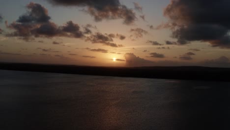 Toma-Aérea-Derecha-De-Camiones-De-Una-Impresionante-Puesta-De-Sol-Dorada-Desde-El-Famoso-Destino-Turístico-Alligator-Beach-En-Un-Gran-Río-En-Cabedelo,-Paraiba,-Brasil,-Cerca-De-La-Capital-Costera-De-Joao-Pessoa