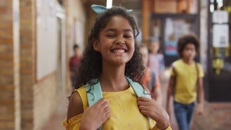 portrait of happy mixed race schoolgirl standing in corridor looking at camera