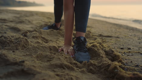 Sportswoman-stretching-reaching-hand-to-leg-outdoor.-Girl-doing-warm-up-on-sand.