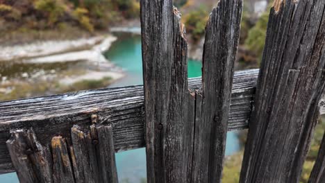 turquoise water of sho river flows in a valley between mountains covered with autumn foliage, seen from an old wooden fence