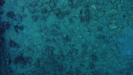 Top-down-close-up-of-turquoise-crystal-clear-water-with-underwater-colorful-rock