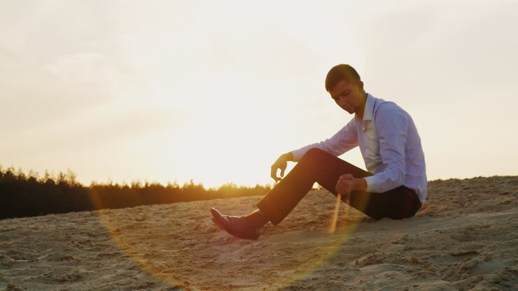 A young businessman holds sand in his hand sitting at sunset on the beach