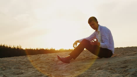 a young businessman holds sand in his hand sitting at sunset on the beach