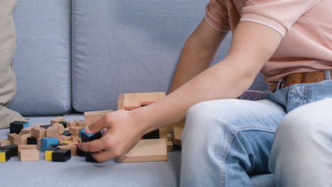 las manos del niño y la mujer jugando con cubos de madera en el sofá en la sala de estar en casa
