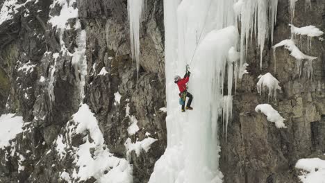 lone ice climber shakes off ice from axe climbing cascade maineline, mount kineo