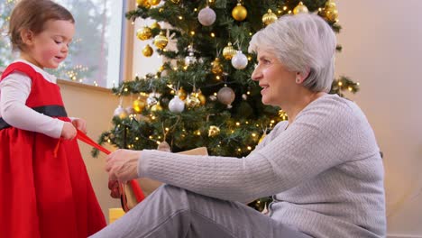 Grandmother-and-Baby-Girl-Opening-Christmas-Gift.christmas,-holidays-and-family-concept-happy-grandmother-and-baby-granddaughter-opening-gift-box-at-home