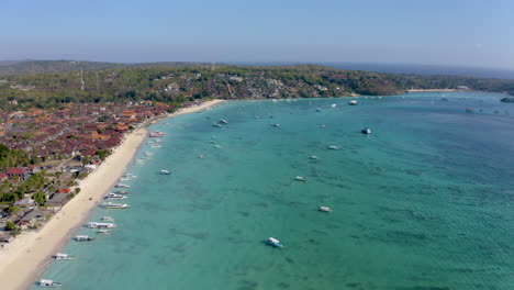 side drone flyover amazing nusa lembongan, jungut batu beach, nusa penida. turquoise ocean with long white sand beach and jungle in background. traditional sailing boat and tropical nature