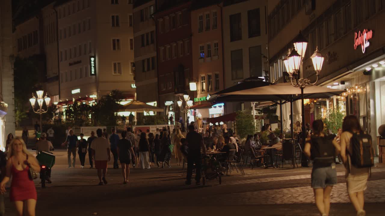 Crowds stroll across illuminated bridge in Nuremberg old town, warm streetlights, steady camera movement