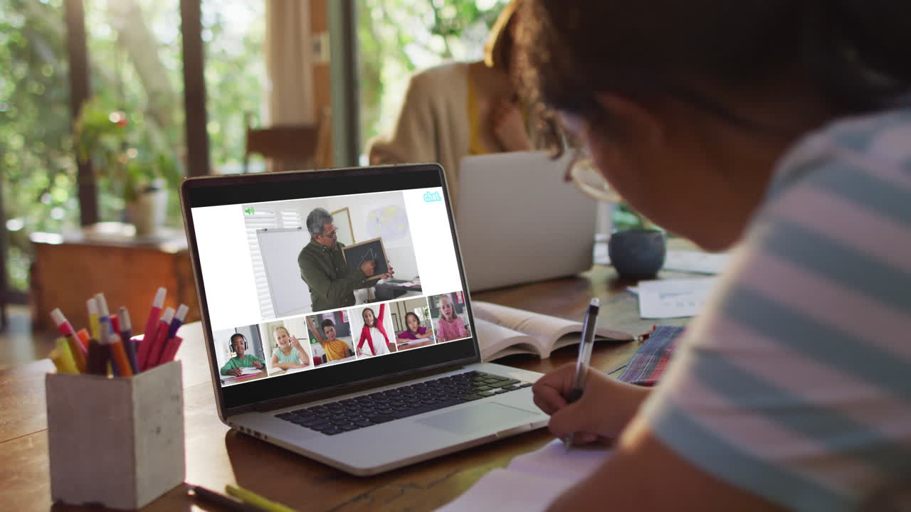 Schoolgirl using laptop for online lesson at home, with diverse teacher and class on screen