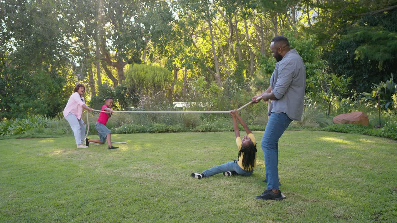 Familia afroamericana jugando a la cuerda en el césped del patio trasero, con un joven de amarillo agarrando la cuerda.