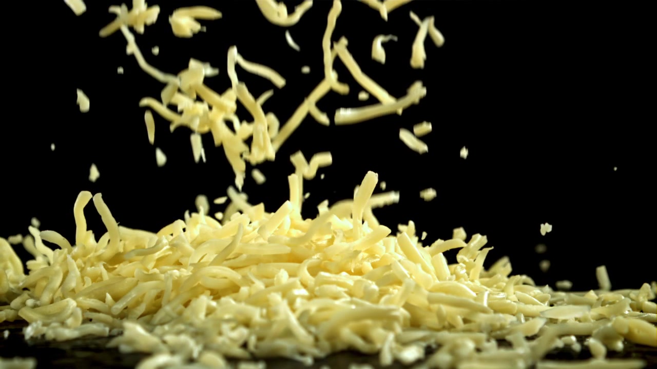 Formaggio grattugiato che cade al rallentatore su uno sfondo nero