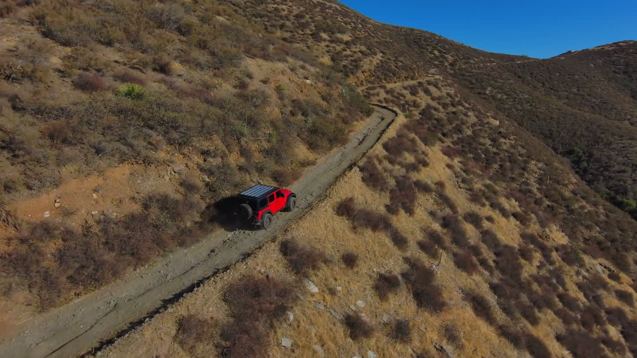 toma aérea de un jeep rojo que viaja por una sinuosa carretera en la ladera de la montaña