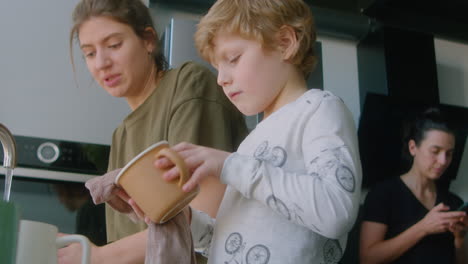 little son helping mother with doing dishes at home
