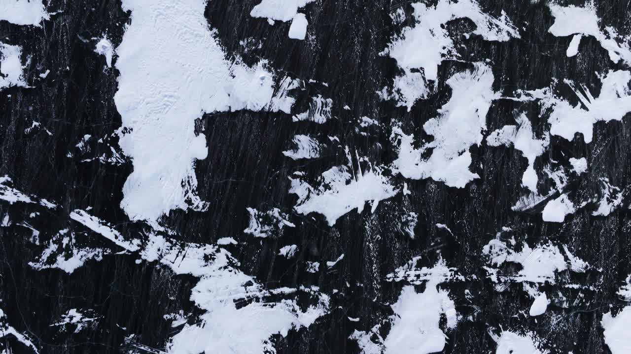 Aerial top down of frozen lake with rough ice texture and scattered snow patches, winter scene, upward motion