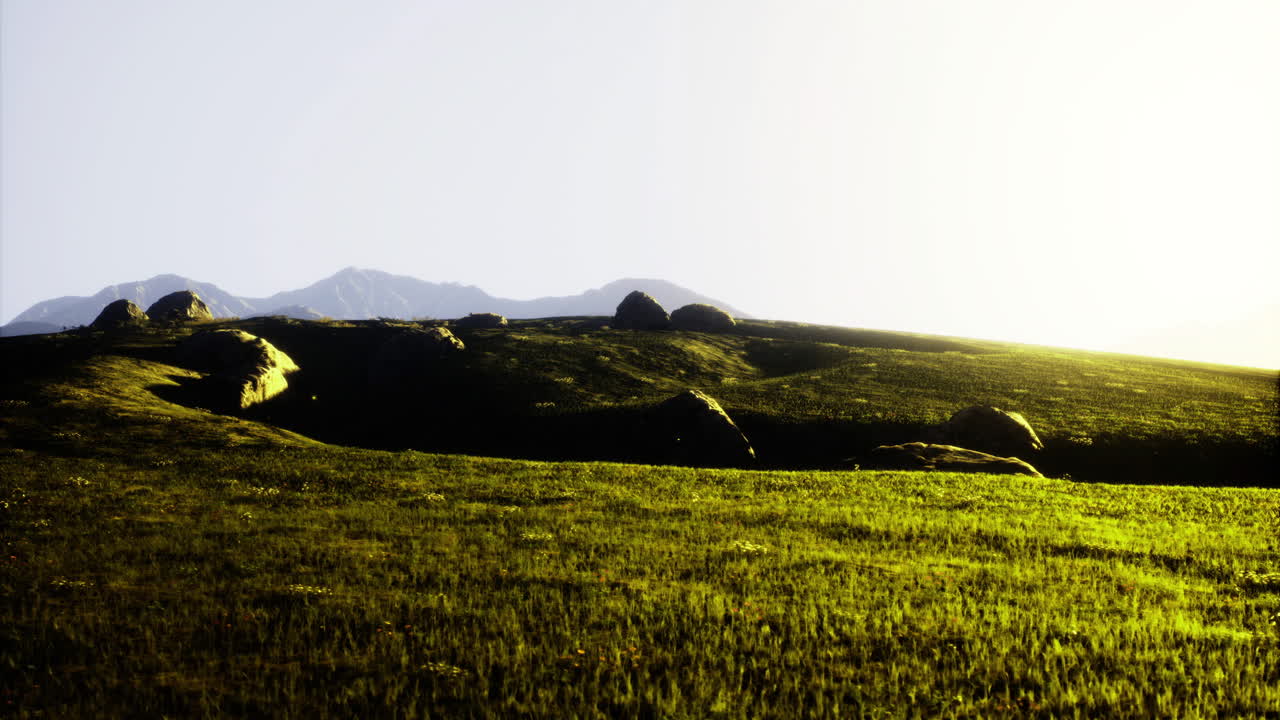 Sunrise over rolling hills with boulders and distant mountains in the backdrop