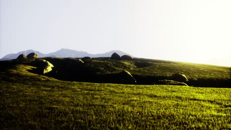 sunrise over rolling hills with boulders and distant mountains in the backdrop